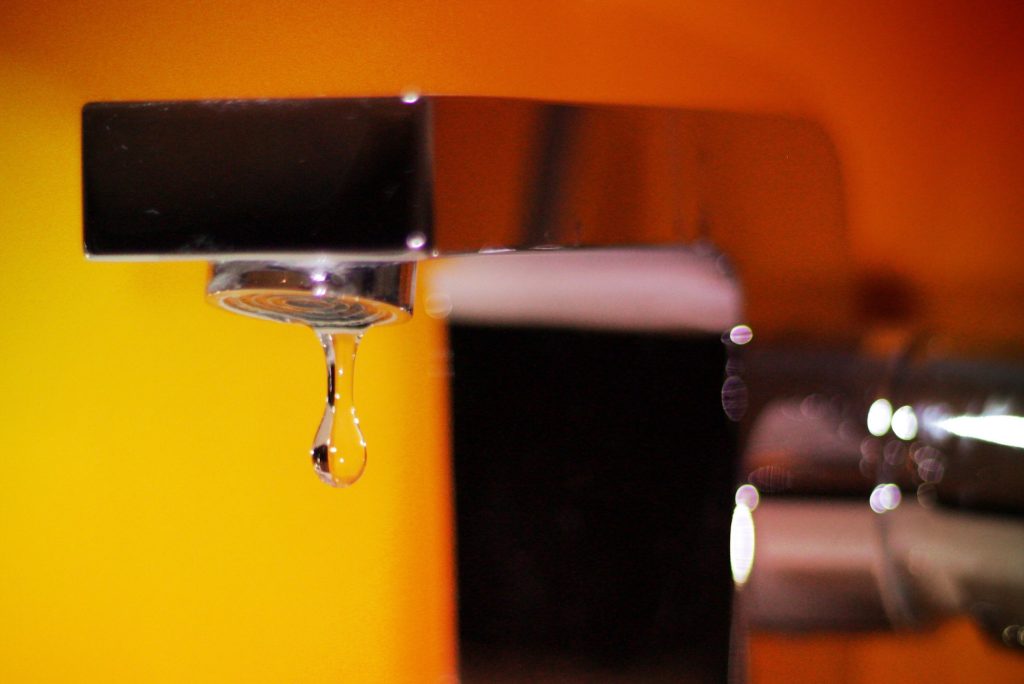 Water drop of a leaking faucet on the orange background